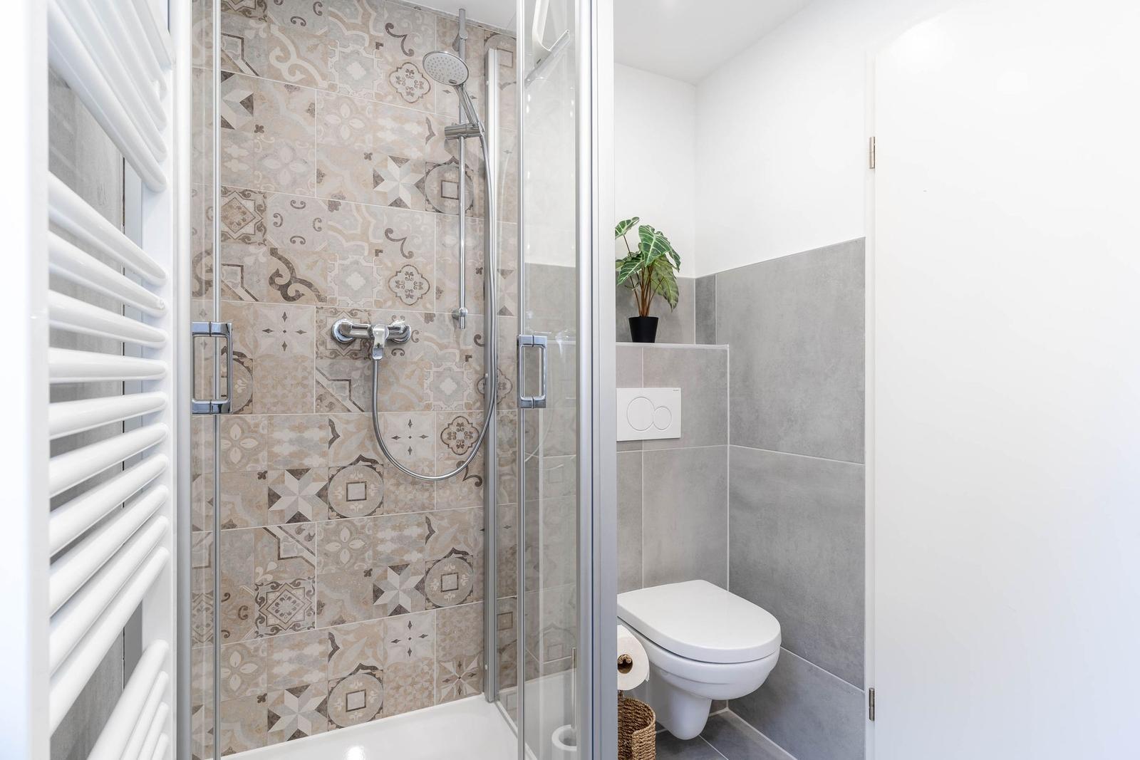 Bad mit Dusche, Toilette und Heizung. Mosaikfliesen an der Duschwand.