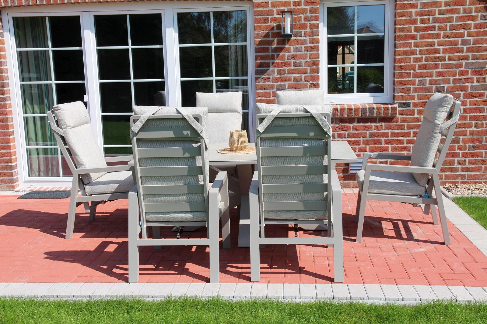 Terrasse mit grauen Gartenstühlen und Tisch vor rotem Backsteinhaus.