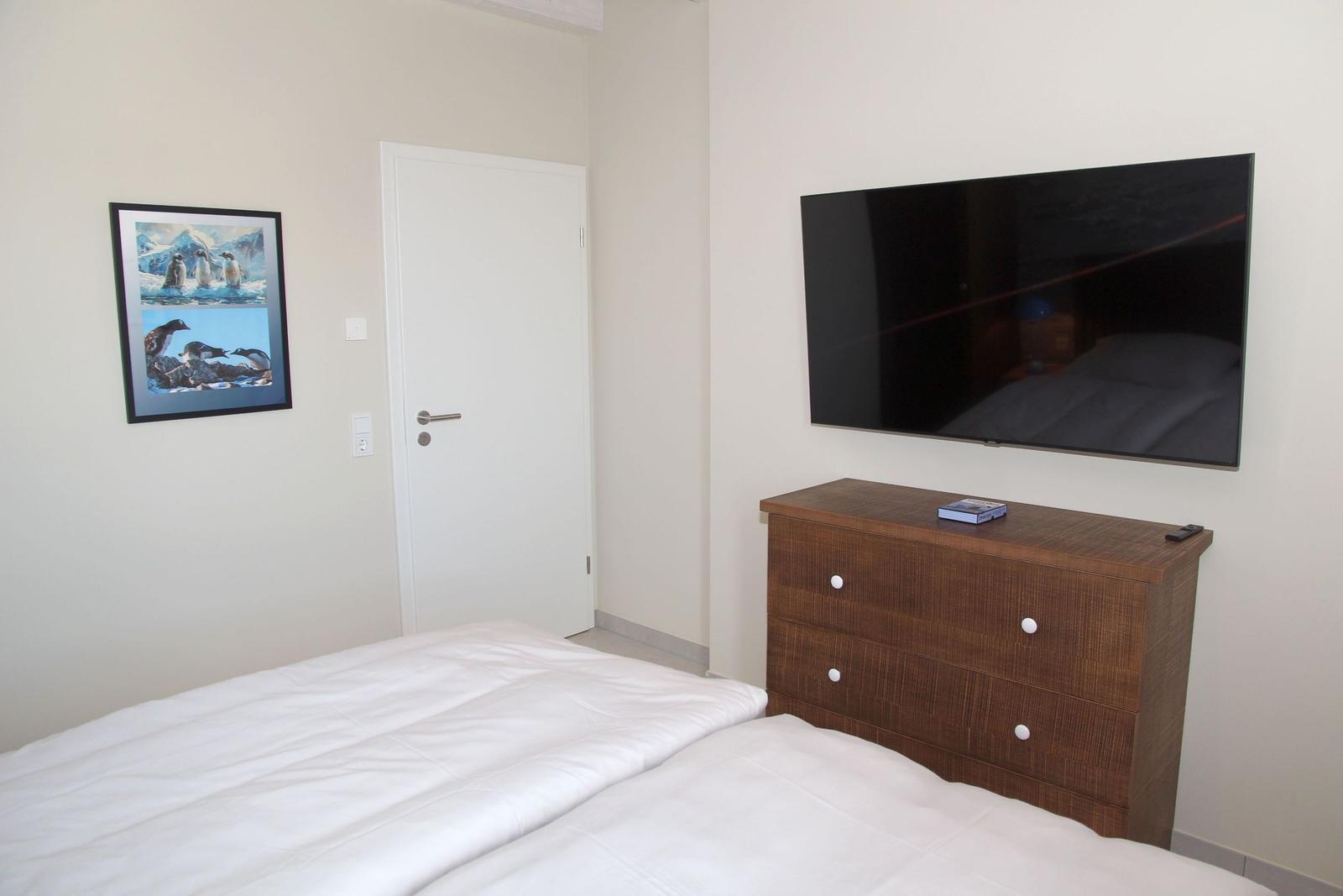 Schlafzimmer mit Bett, Kleiderschrank und Wandbild. Flachbildfernseher an der Wand.