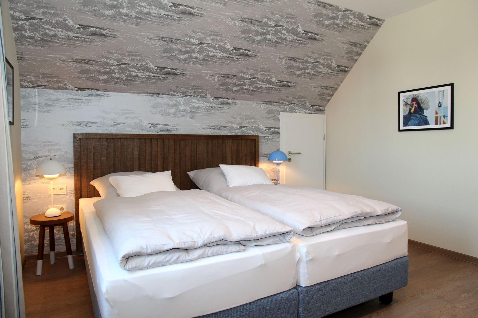 Zimmer mit Doppelbett, Wellenmusterwand und zwei Nachttischen mit Lampen.