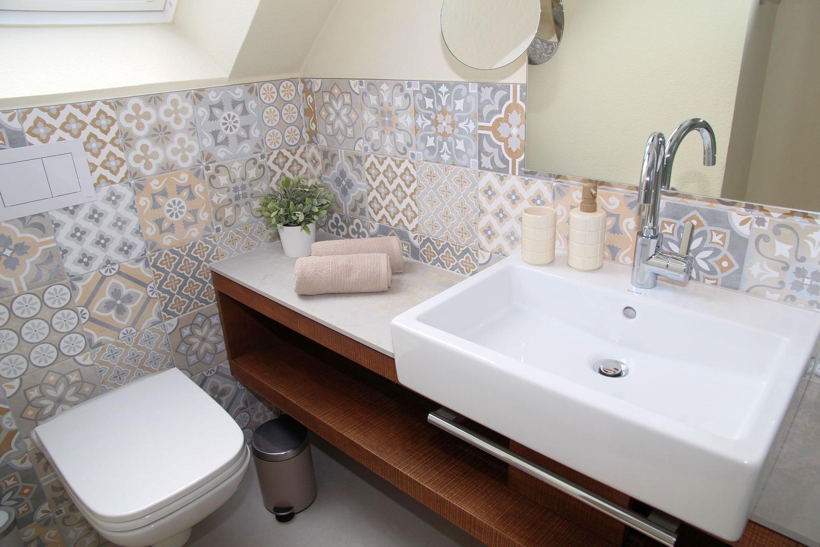 Badezimmer mit Waschbecken, Toilette und dekorativen Fliesen an der Wand.