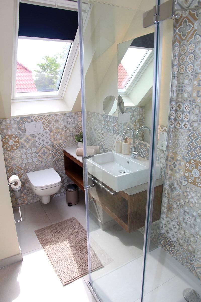 Badezimmer mit Dusche, Waschbecken und Toilette unter Dachfenster.