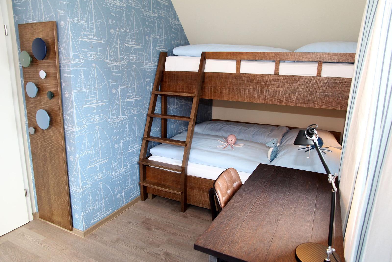 Ein Schlafzimmer mit Doppelstockbett, Schreibtisch und Segelyacht-Wandtapete.