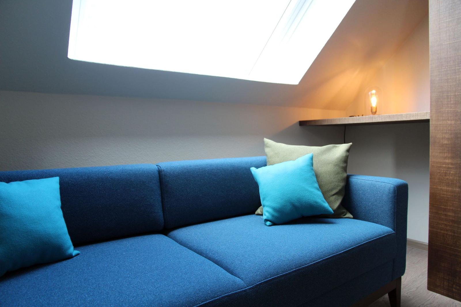 Blauer Sofa mit Kissen unter Dachschrägen und Dachfenster.