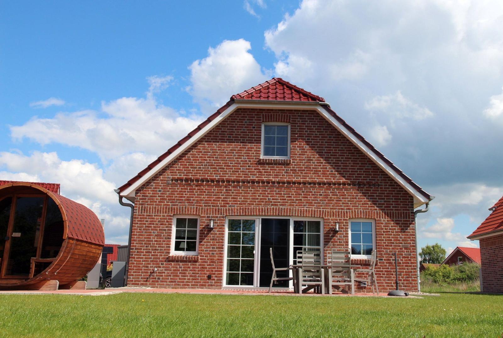 Rotes Ziegelhaus mit Terrasse und Garten. Links steht ein runder Holzschuppen.