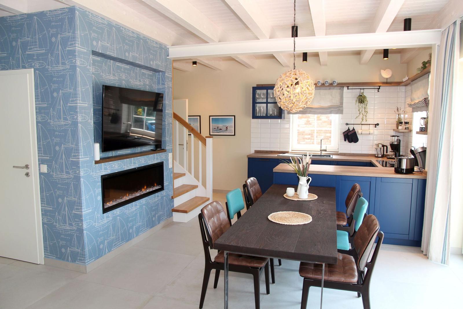 Essbereich mit Tisch und Stühlen, Küche mit blauen Schränken und Wand mit Segelyacht-Motiv.