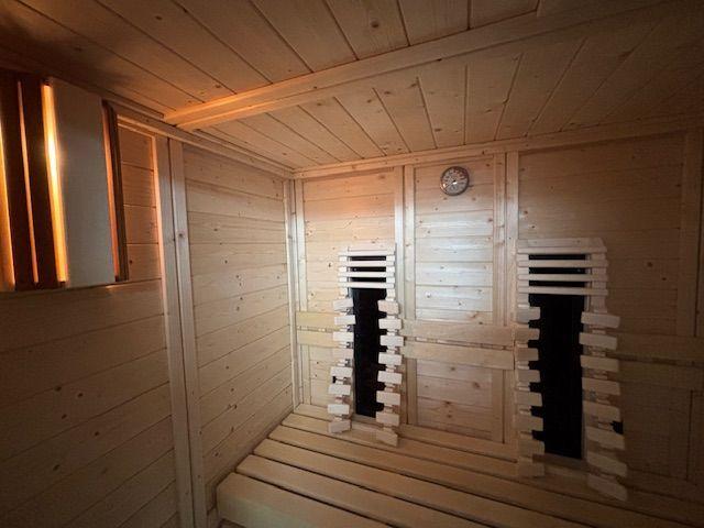 Sauna with wooden cladding, benches, and heater. Wall clock and light strip visible.