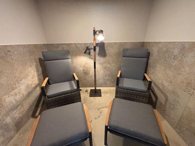 Two chairs with footrests and a floor lamp in a room with tiled walls.