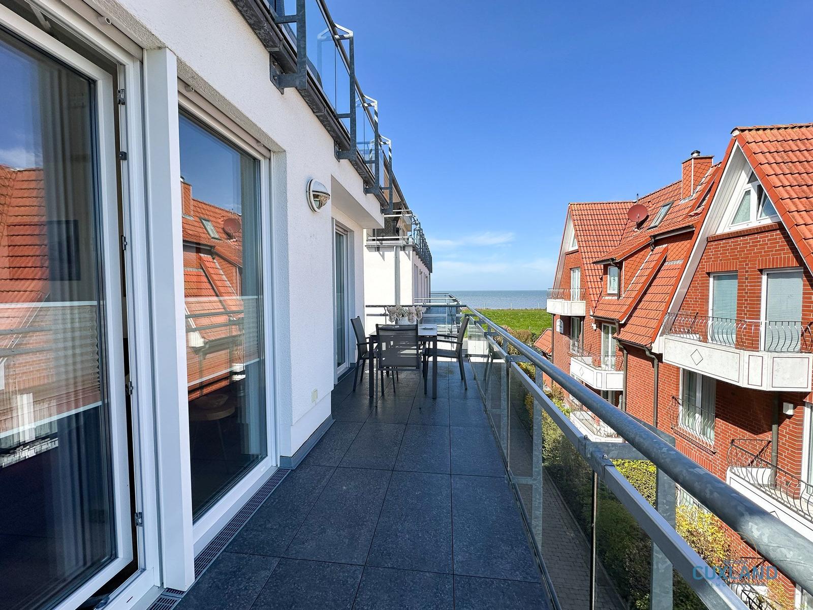 Terrasse mit Tisch und Stühlen, Blick auf Meer und rote Dächer.