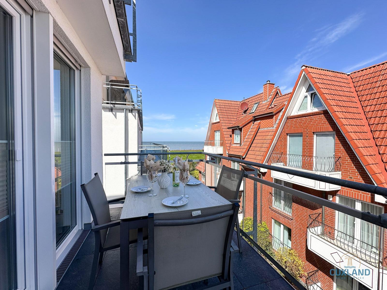 Terrasse mit Tisch und Stühlen, Blick auf rote Dächer und Meer.