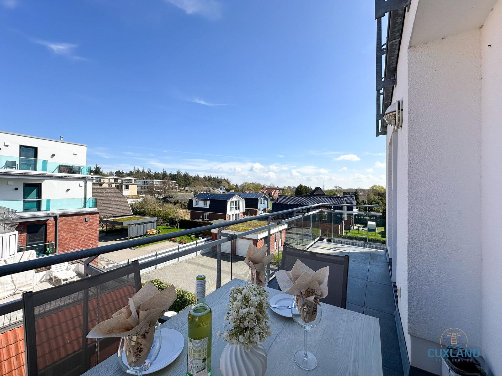 Terrasse mit Tisch, Stühlen und Blick auf Wohngebiet und Himmel.