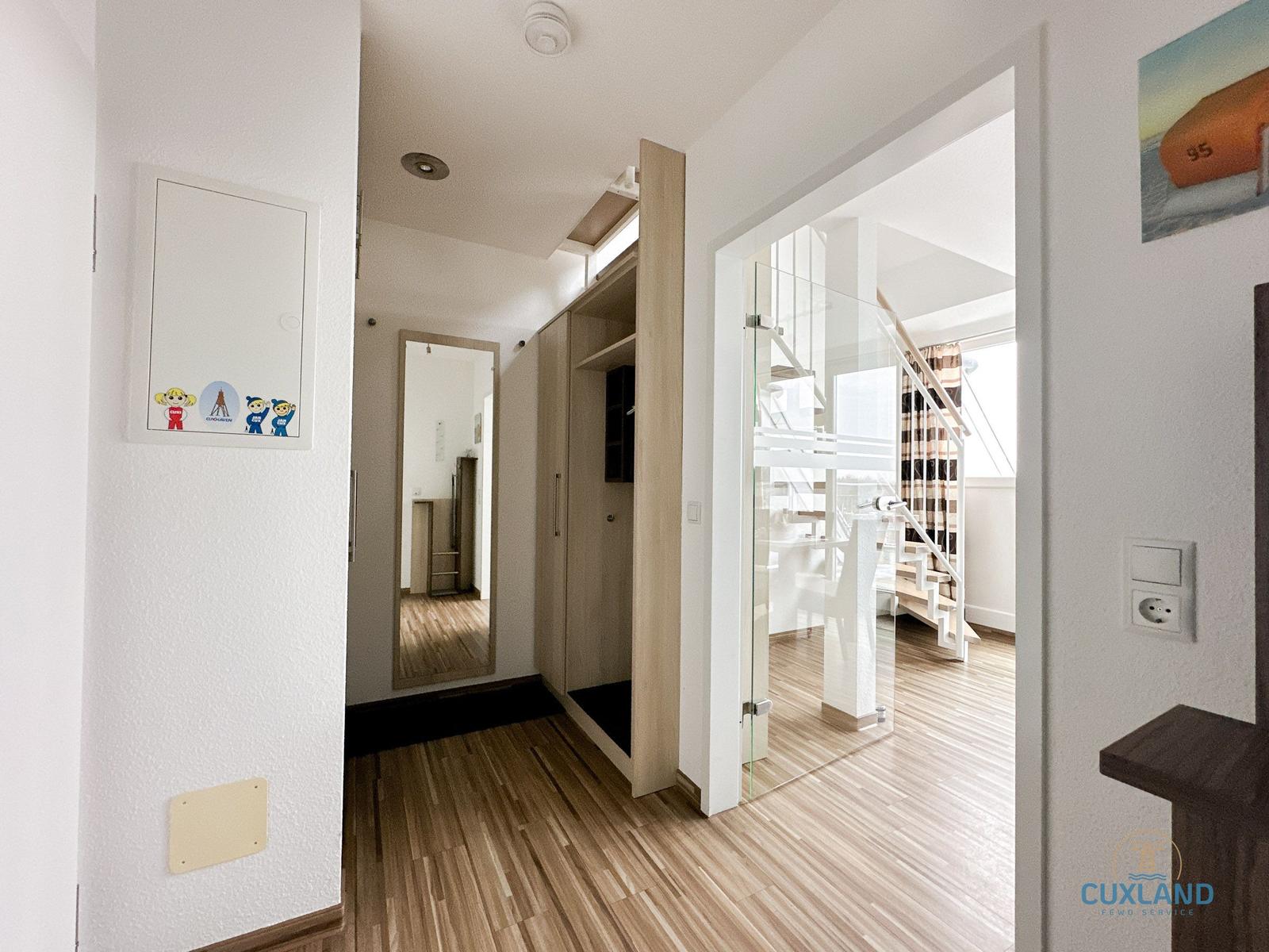 Hausflur mit Garderobe, Spiegel und Glasgeländer zur Treppe.