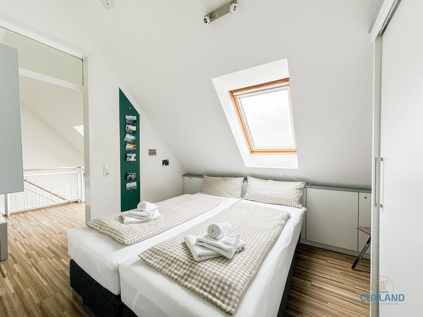 Zimmer mit Doppelbett, Dachfenster und Holzboden. Blick in angrenzenden Raum.