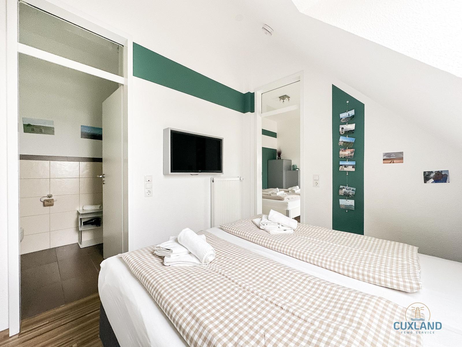Schlafzimmer mit Doppelbett, Fernseher und angrenzender Dusche.