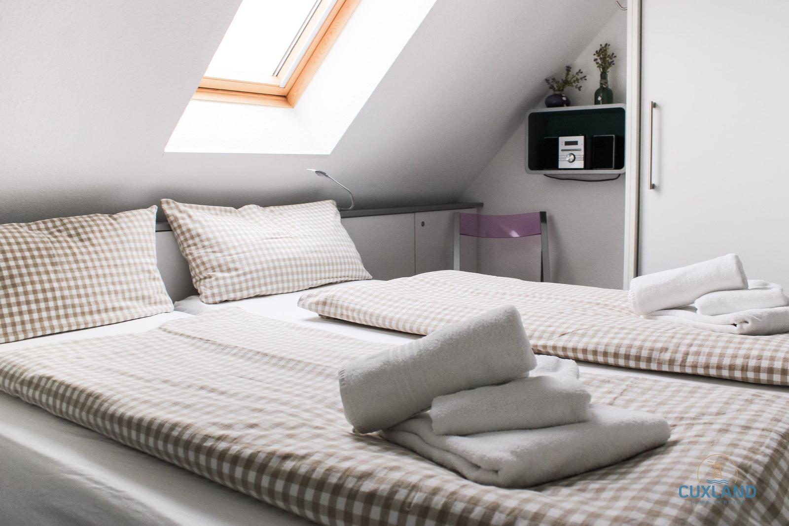 Zimmer mit Dachschrägen, Doppelbett und Dachfenster. Handtuch auf dem Bett.