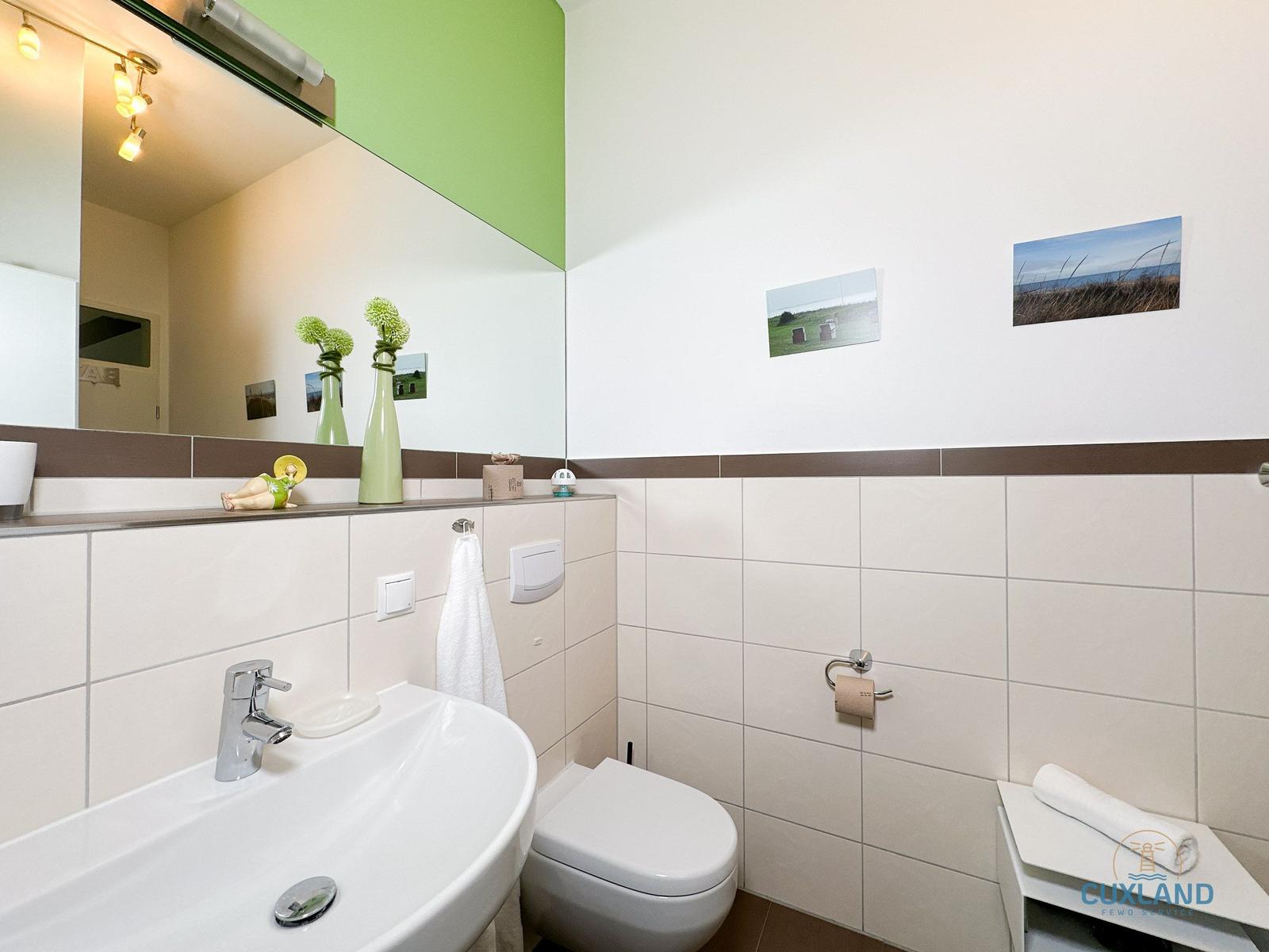Badezimmer mit Waschbecken, Toilette und Spiegel. Wand mit grüner Farbe und Bildern.