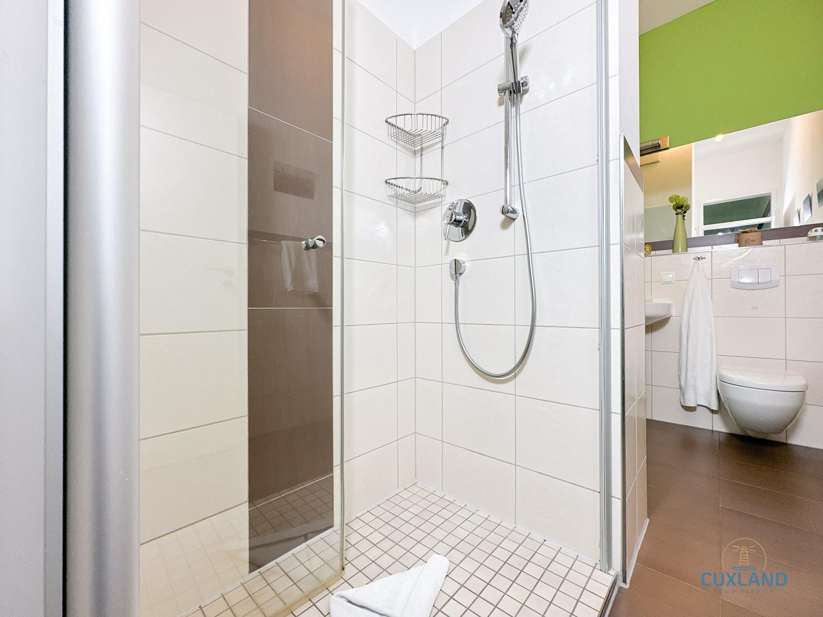 Dusche mit Duschbrause, Handtuch und Aufbewahrungskörben. WC und Waschbecken im Hintergrund.