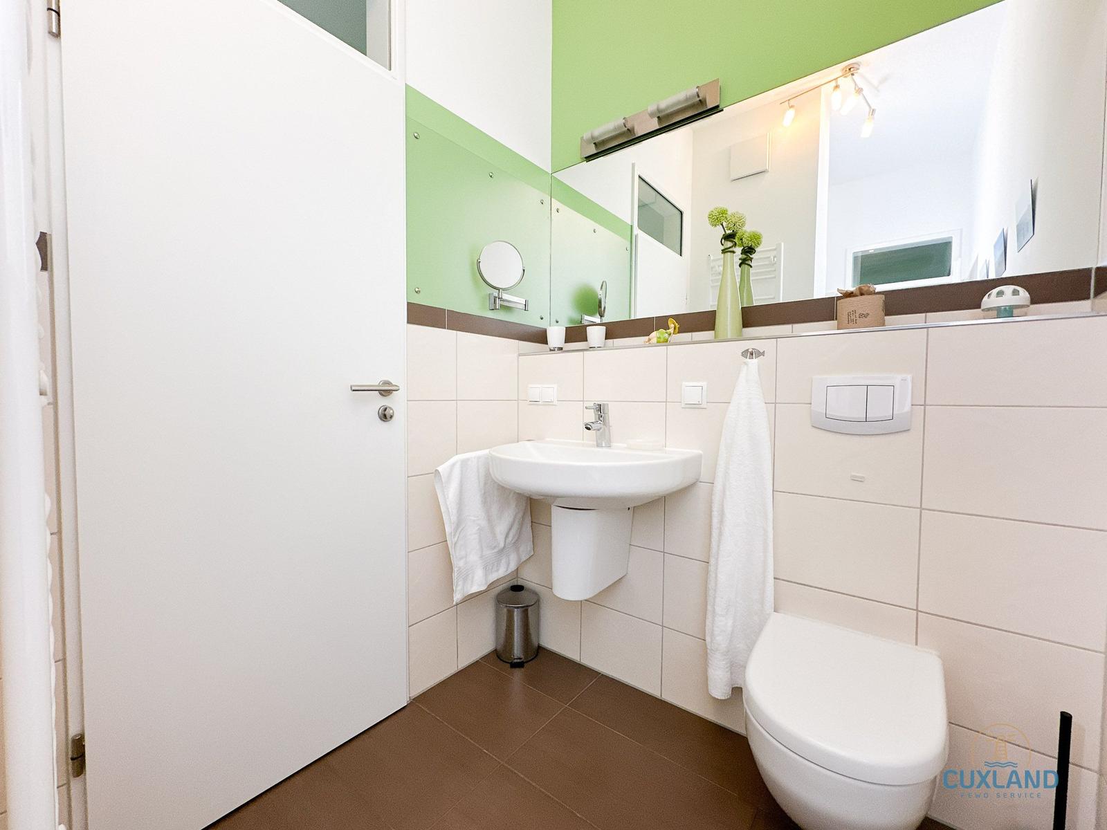 Badezimmer mit Waschbecken, Toilette und Spiegel. Wandfarbe grün-weiß.