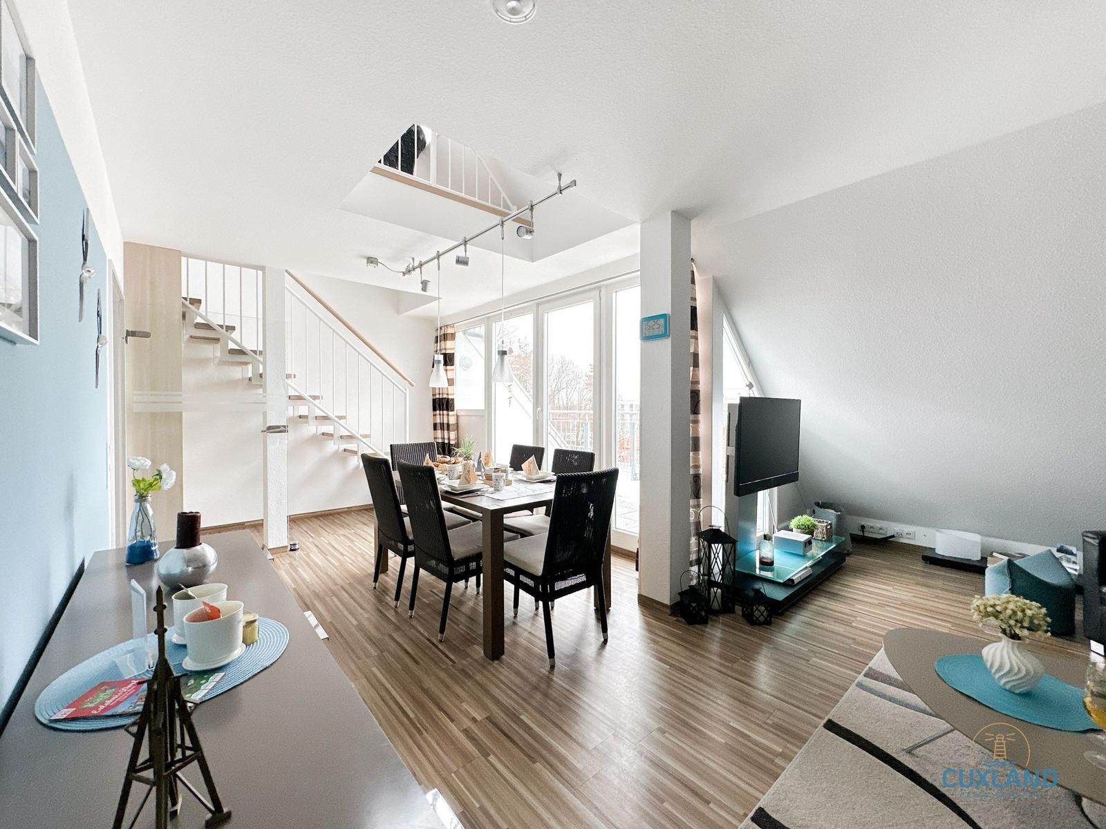 Esszimmer mit Tisch, Stühlen und TV. Hintergrund: Treppe und Fenster.