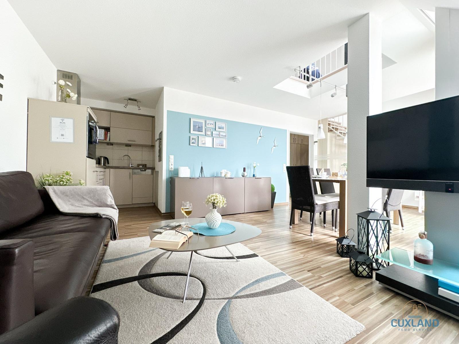 Wohnzimmer mit Sofa, Couchtisch und Fernseher. Küche und Essbereich sind sichtbar.