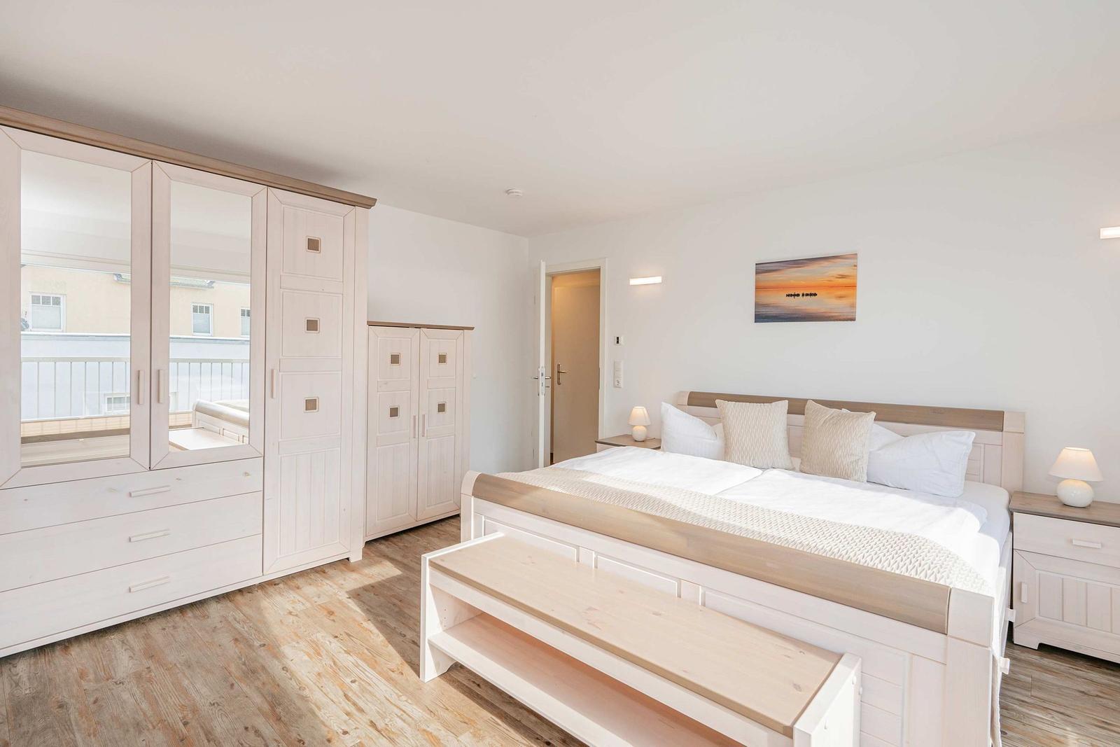 Schlafzimmer mit Doppelbett, Kleiderschrank und Nachttischen. An der Wand hängt ein Bild.