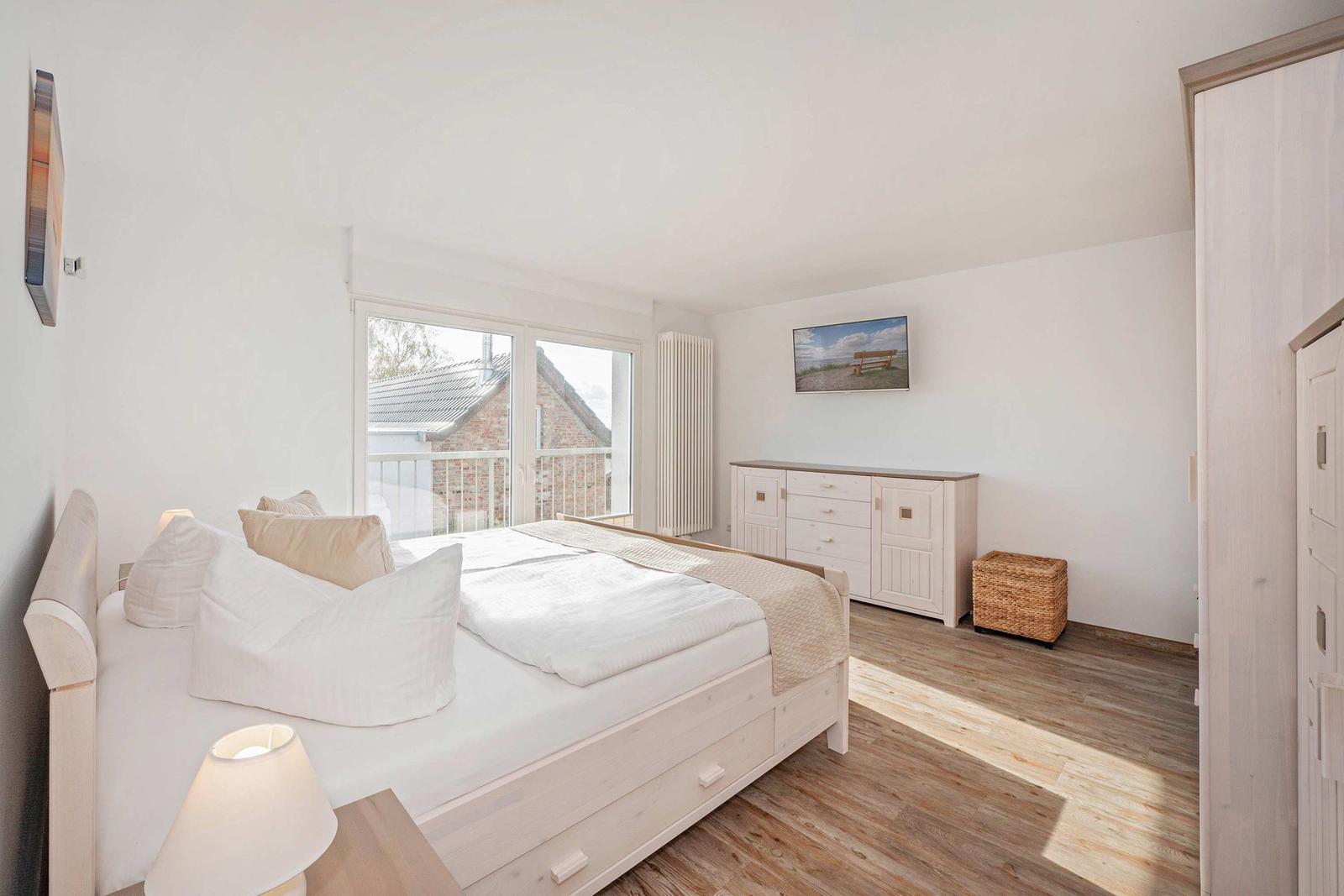 Schlafzimmer mit Bett, Schrank und Fenster zum Balkon
