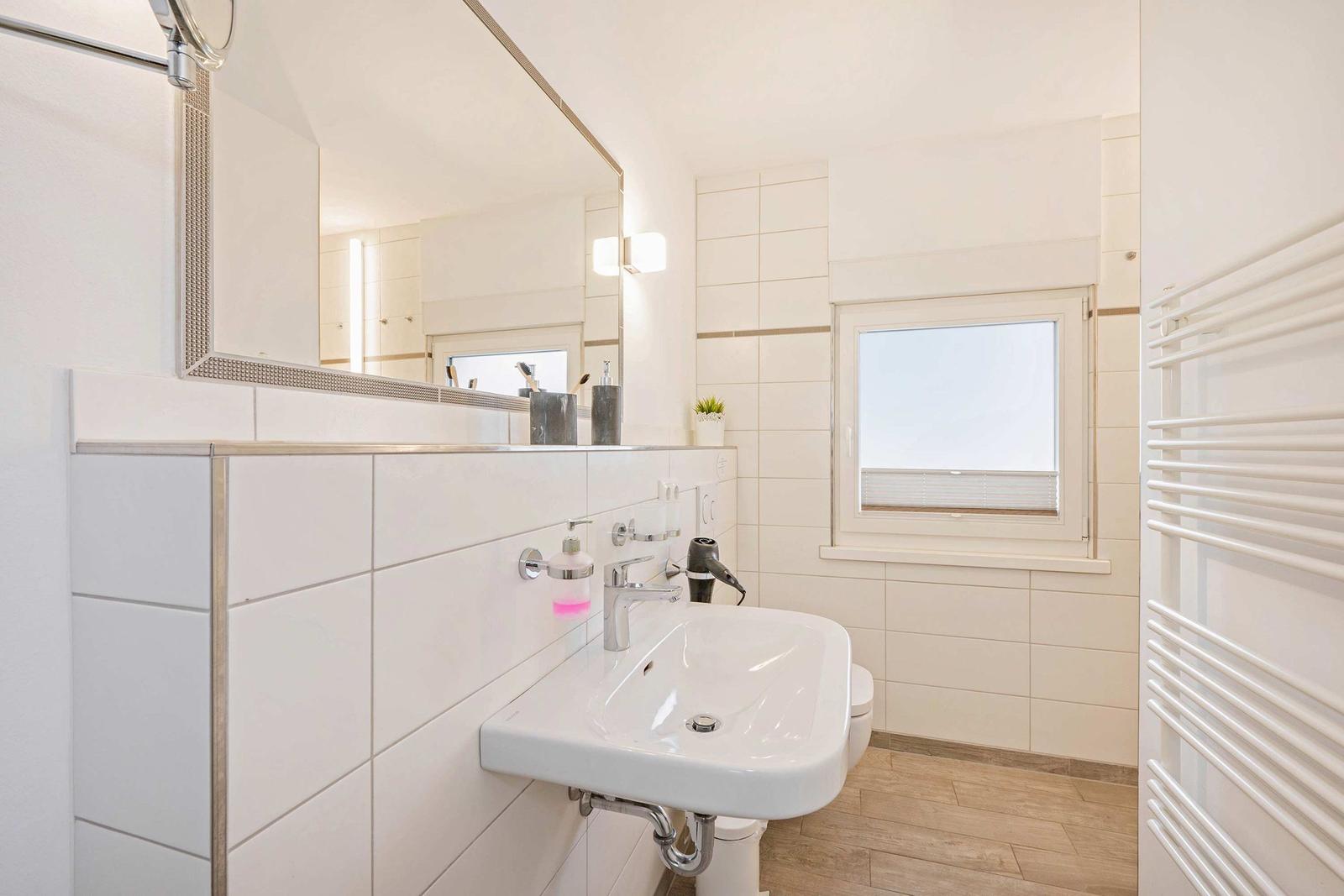 Badezimmer mit Waschbecken, Spiegel, Fenster und Heizung.