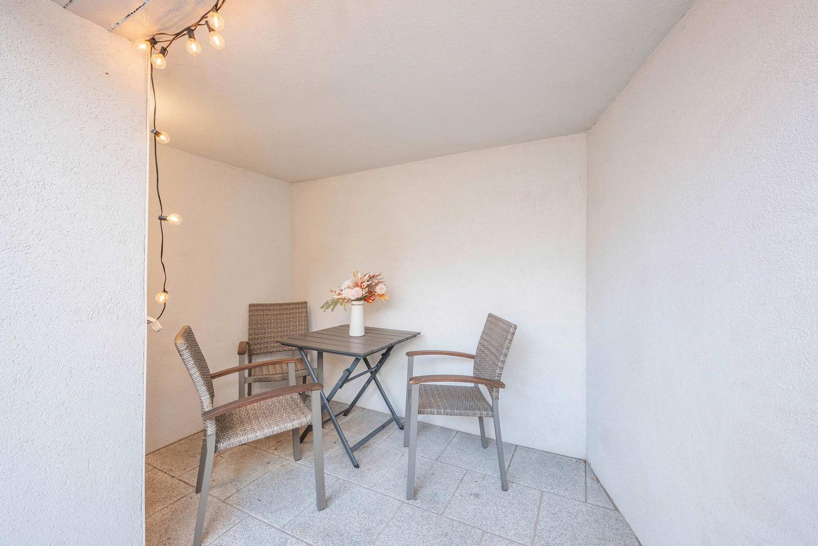 Terrasse mit Tisch, drei Stühlen und Blumenvase. Lichterkette an der Wand.