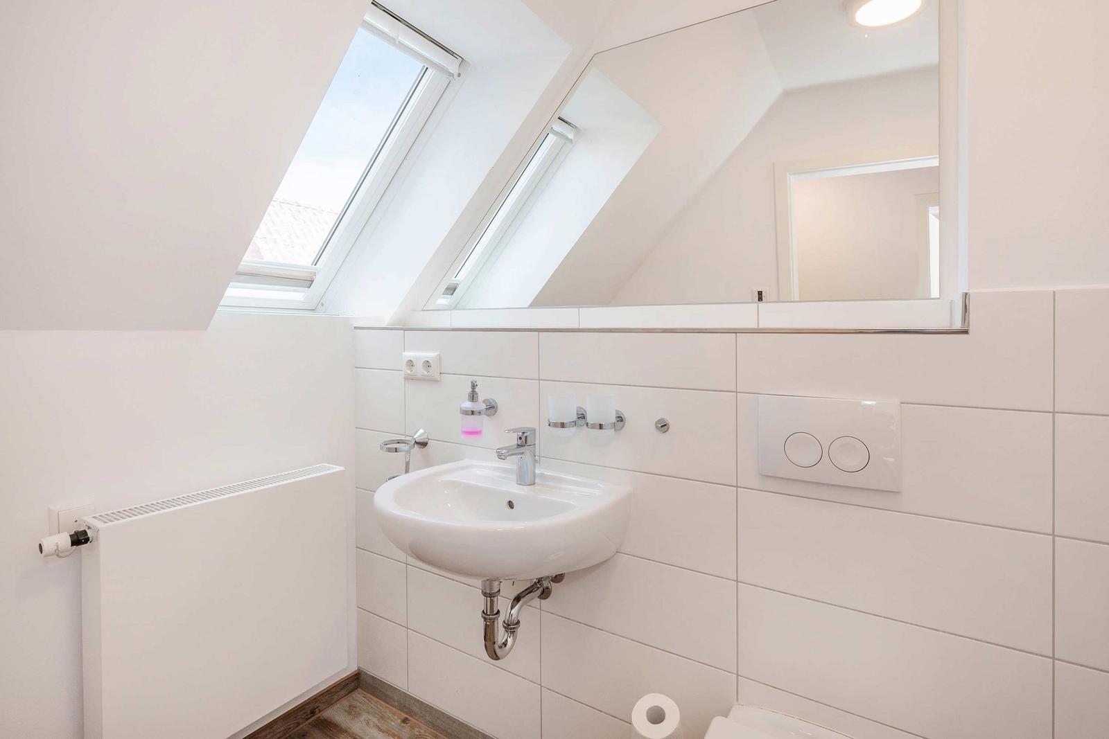 Badezimmer mit Dachfenster, Spiegel und Waschbecken.