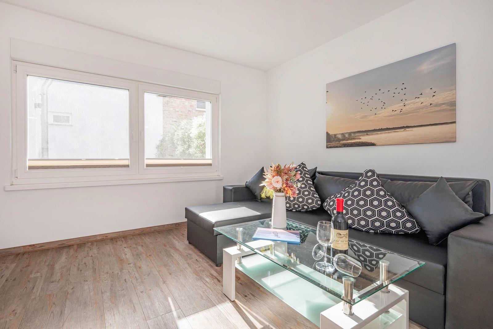 Wohnzimmer mit grauem Sofa, Glas-Tisch und Wandbild mit Vögeln.