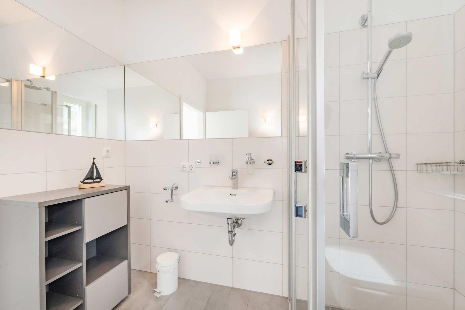 Badezimmer mit Dusche, Waschbecken und Spiegeln an den Wänden.