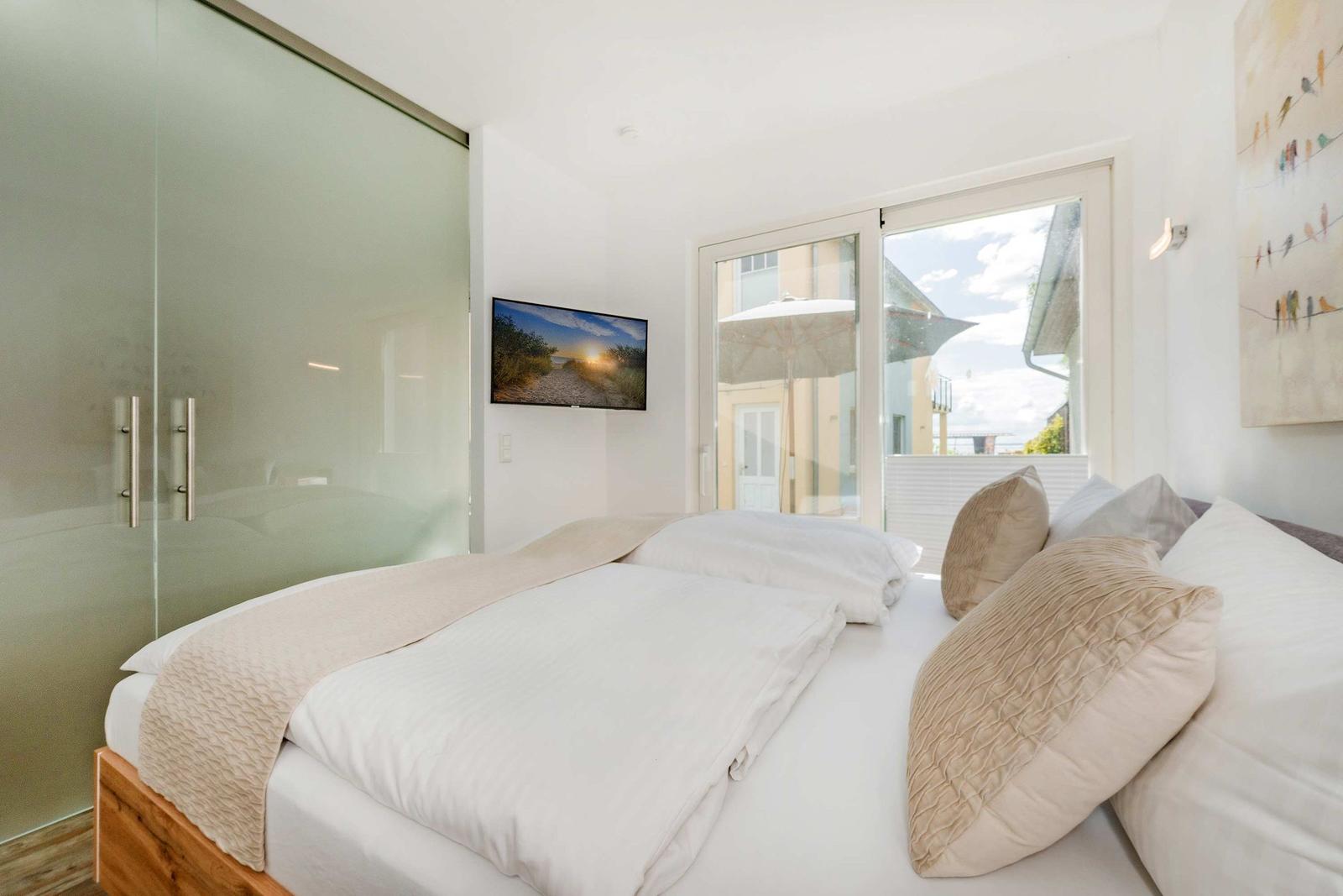 Schlafzimmer mit Doppelbett, Glaswand und Fenster zur Terrasse.
