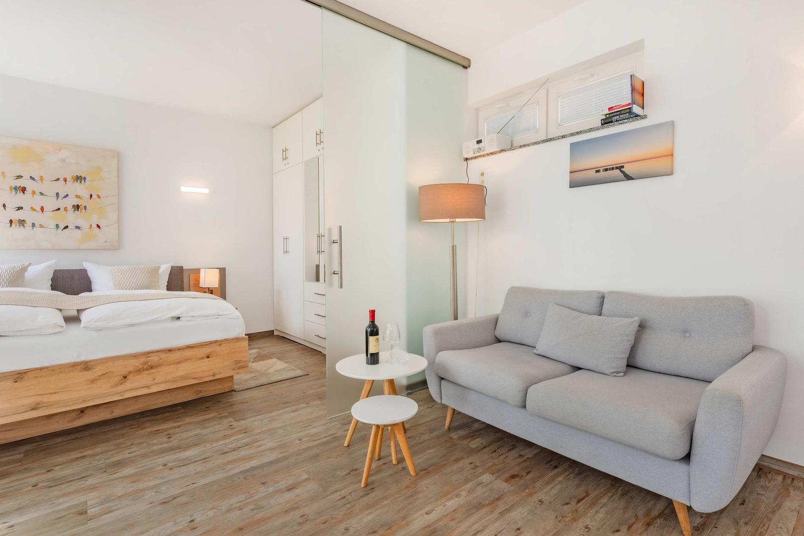 Schlafzimmer mit Bett, Sofa und Kleiderschrank. Holzboden und Wandbilder.