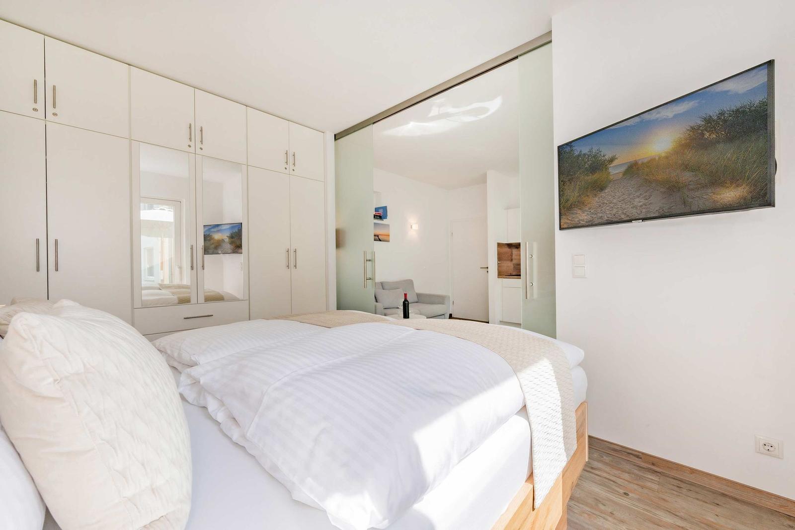 Schlafzimmer mit Doppelbett, weißen Schränken und Fernseher an der Wand.