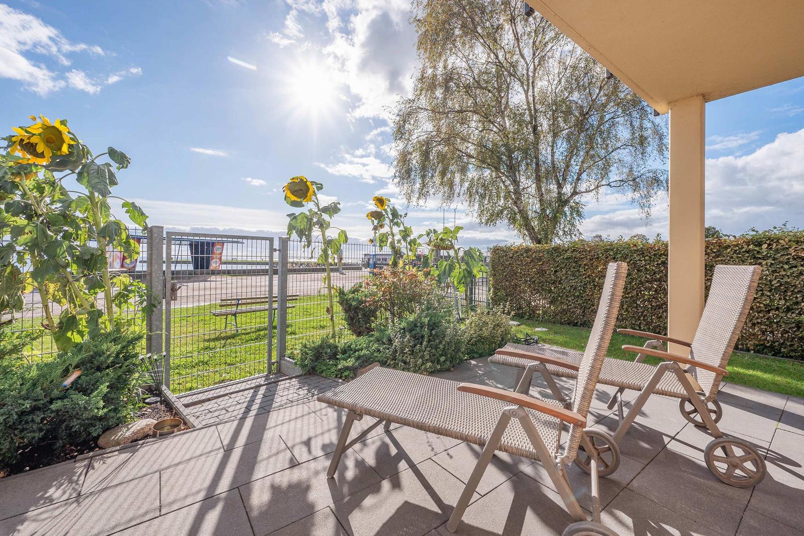 Terrace with sun loungers, sunflowers, and view of green area.