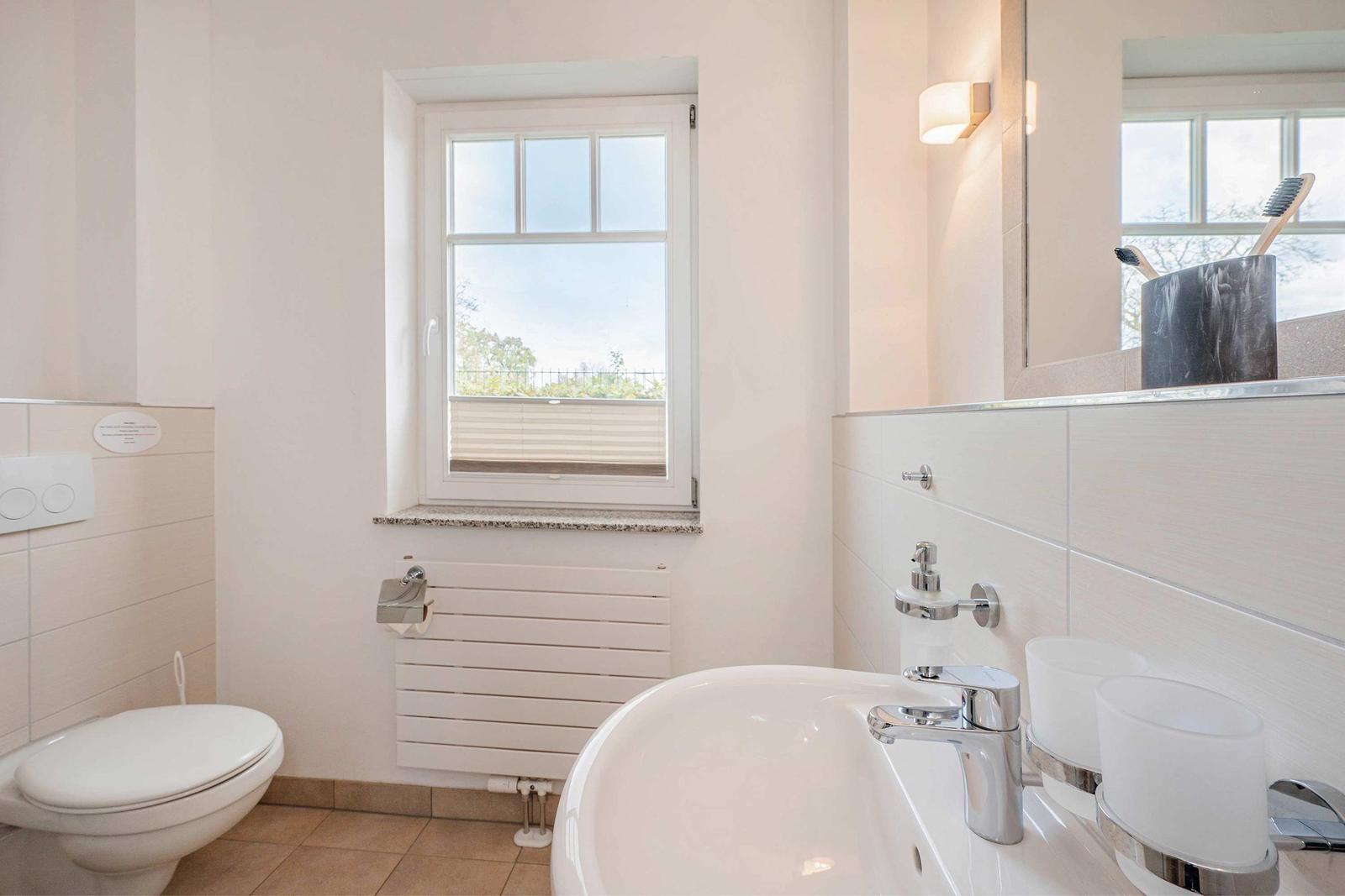 Bathroom with toilet, sink, and window with view outside.