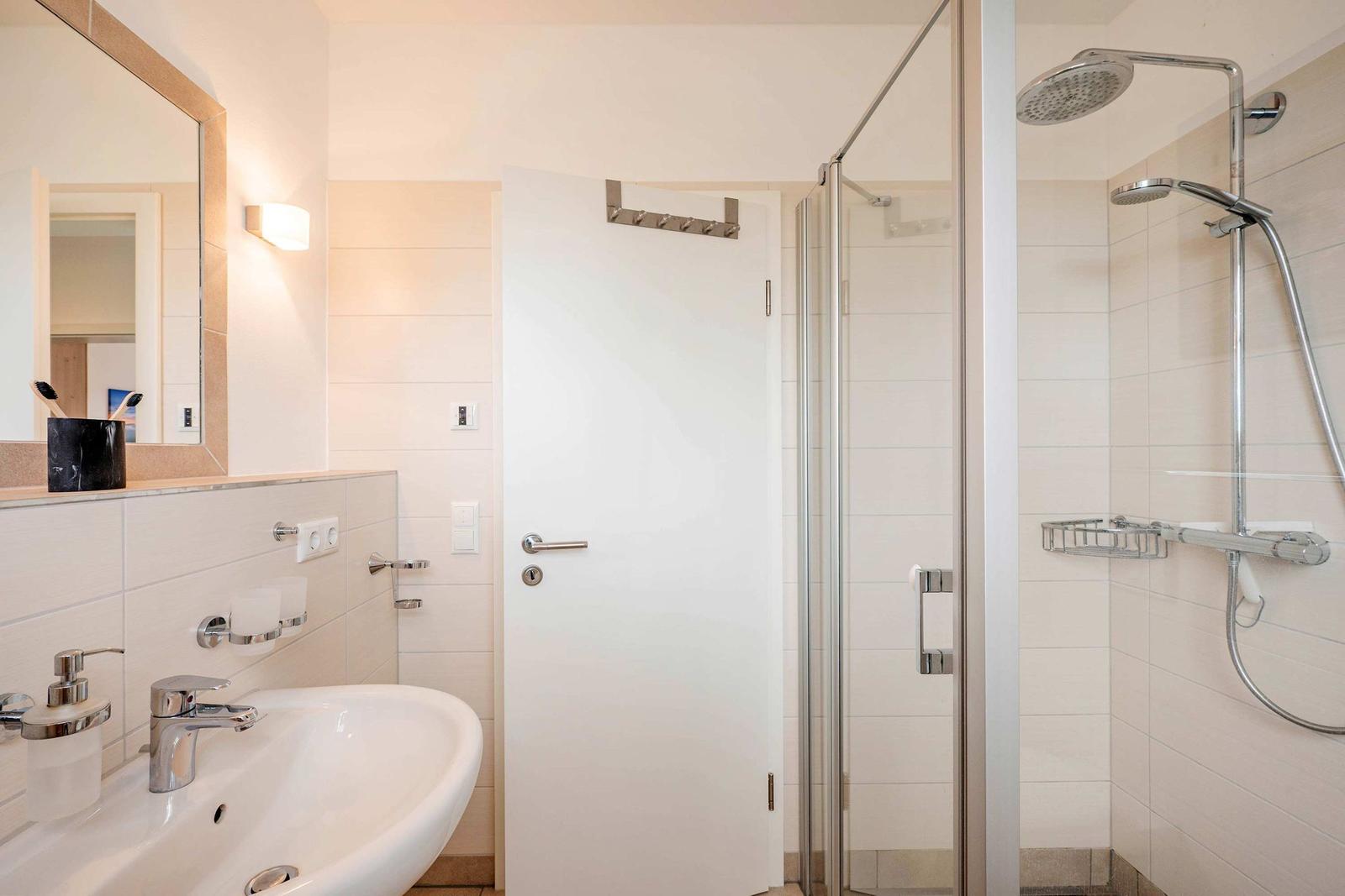 Bathroom with shower, sink, and mirror. Tiled wall and modern fixtures.
