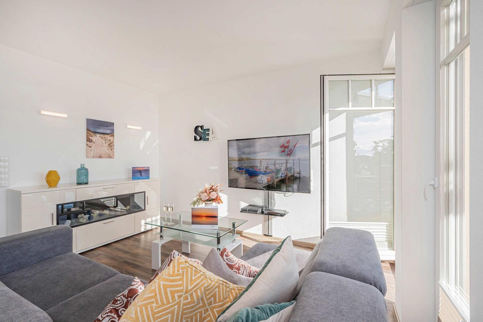 Living room with sofa, TV, and glass table. Passage to terrace with water view.