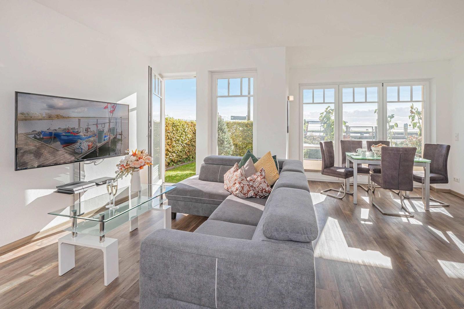 Living and dining area with large sofa, glass table, and view of garden.