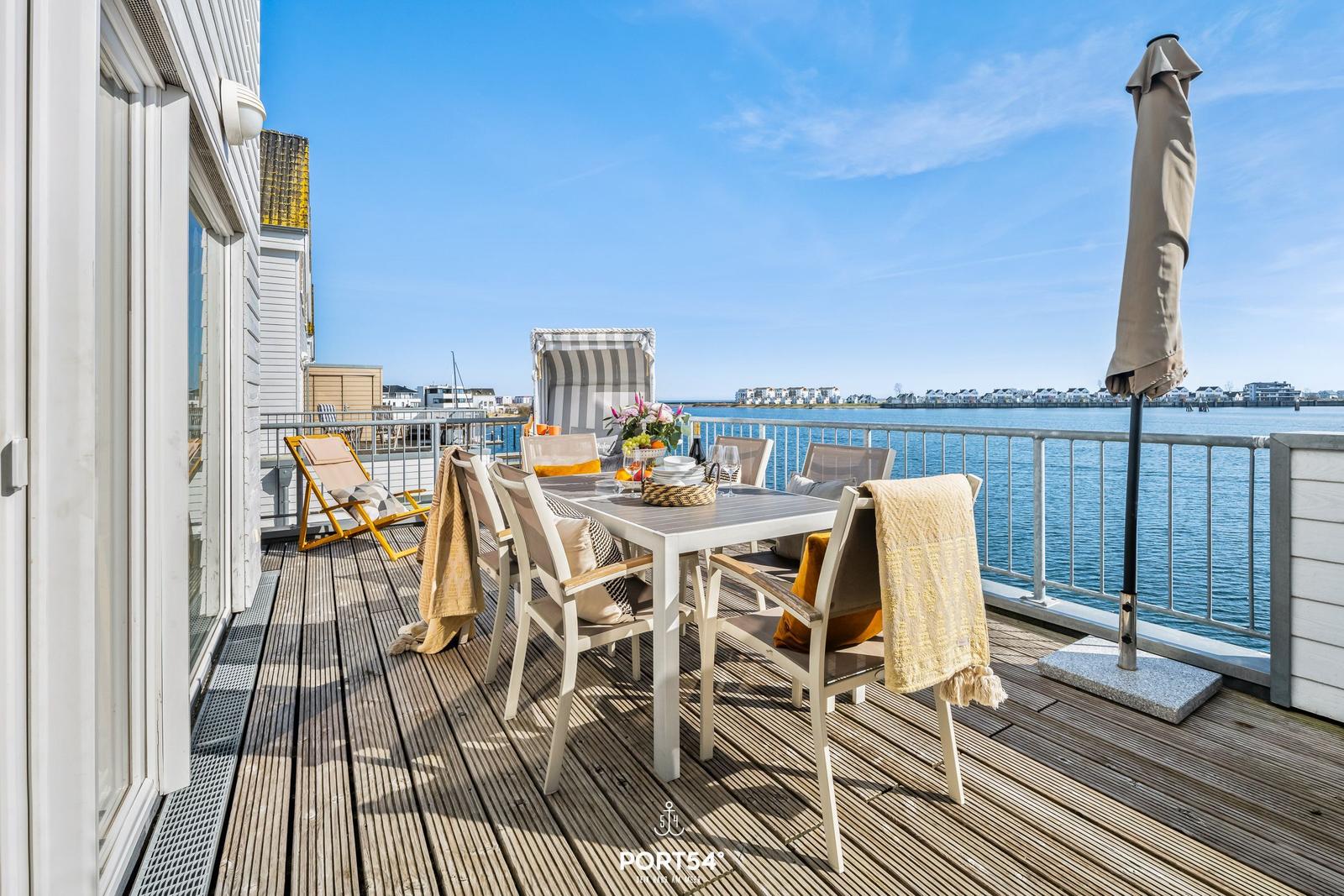 Terrasse mit Tisch, Stühlen und Blick aufs Wasser.