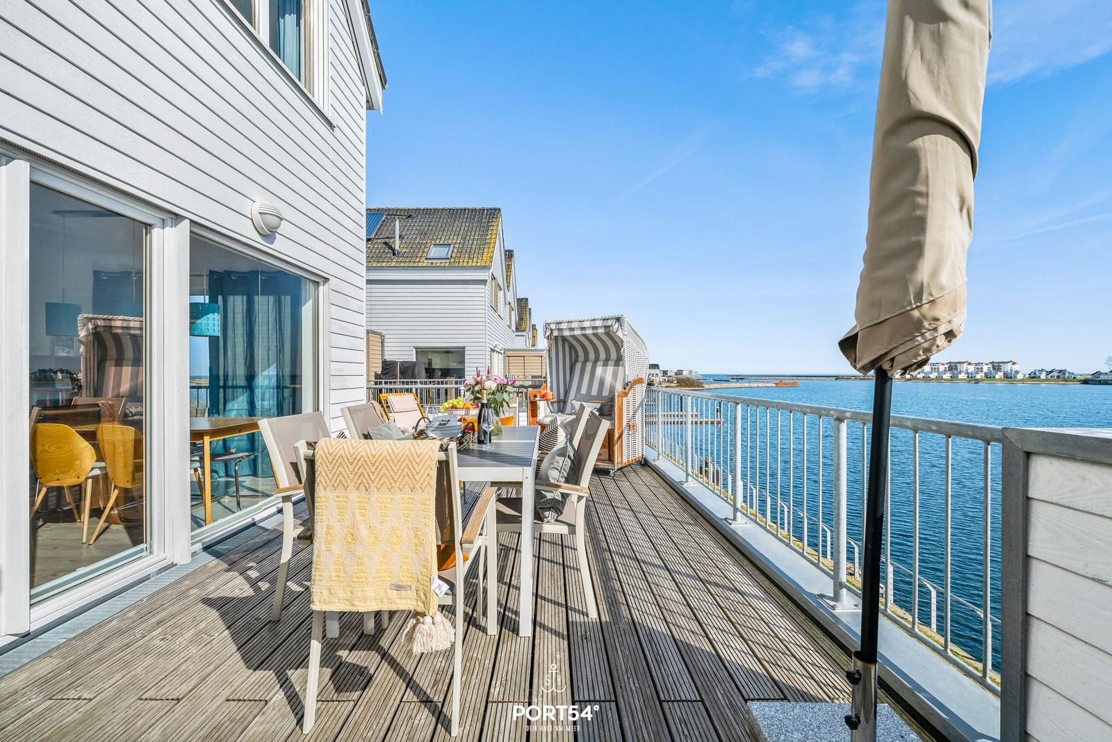 Terrasse mit Tisch, Stühlen und Blick auf Wasser.