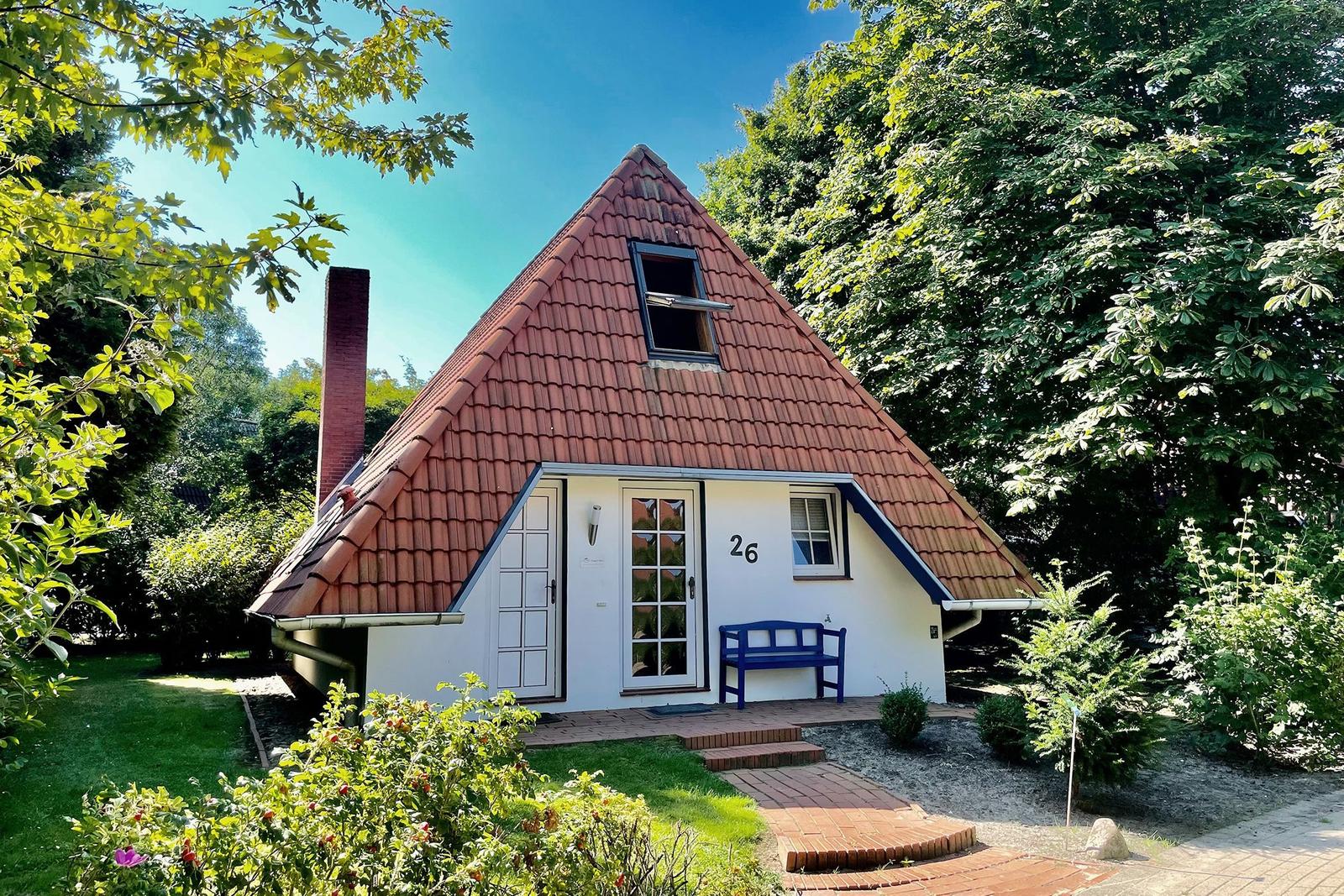 A white house with a red roof, blue bench, and garden.