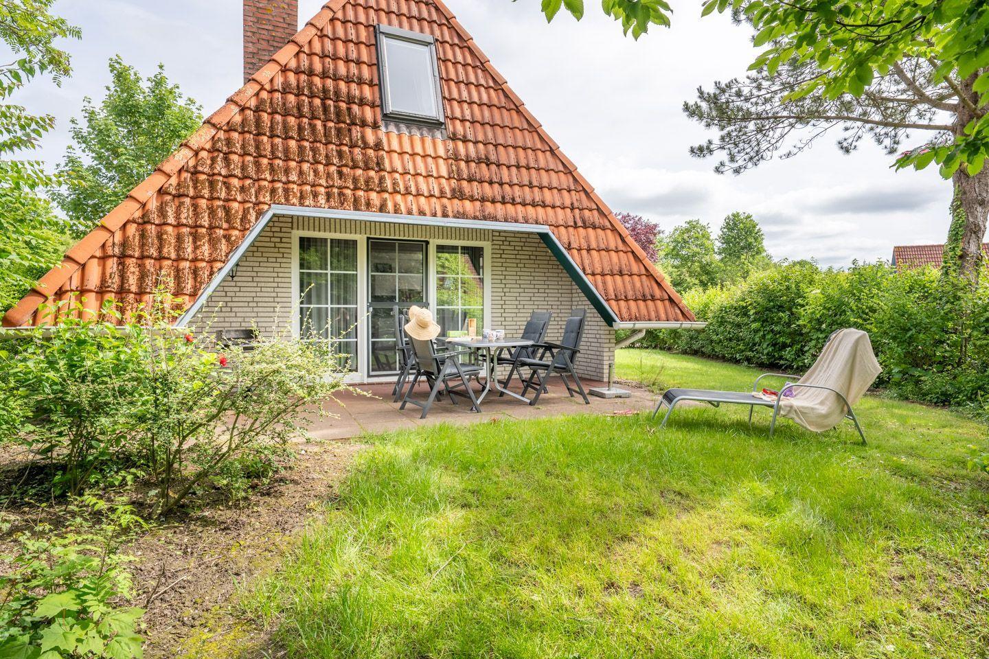 Haus mit Terrasse, Garten und Liegestuhl. Holzverkleidung und rote Ziegeldach.