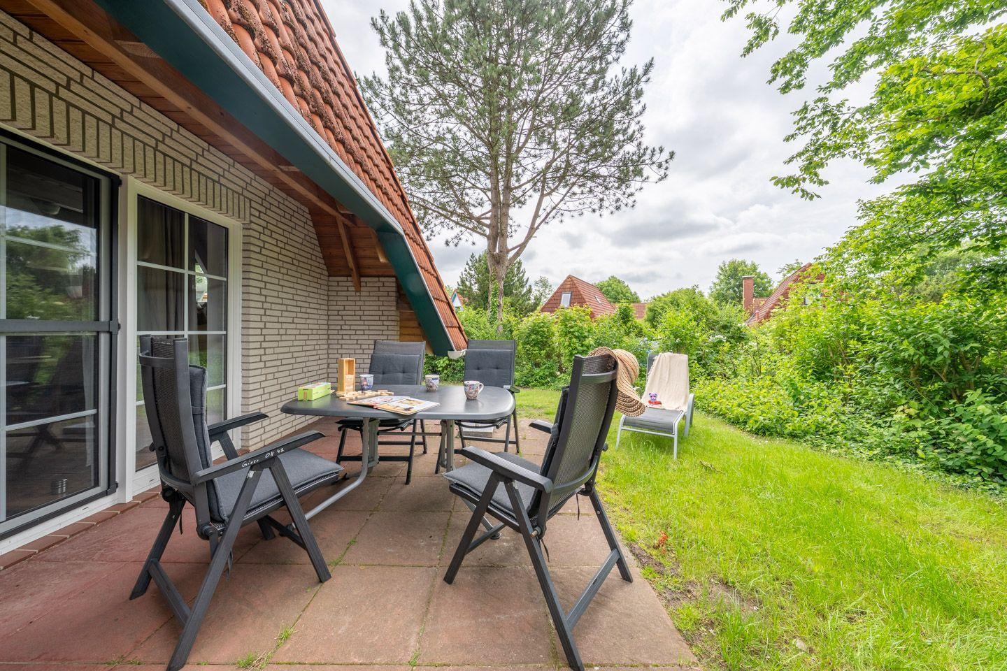 Terrasse mit Tisch und Stühlen, Grünfläche und Baum im Hintergrund.