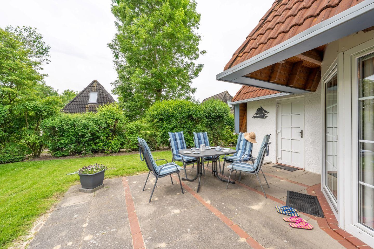 Terrace with table and chairs, garden, house with door and window.
