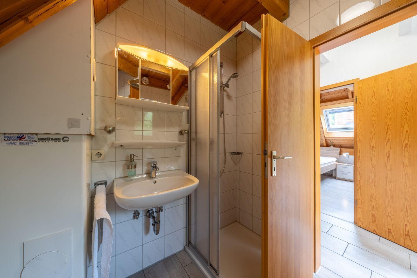 Bathroom with shower, sink, and mirror. Door leads to bedroom.