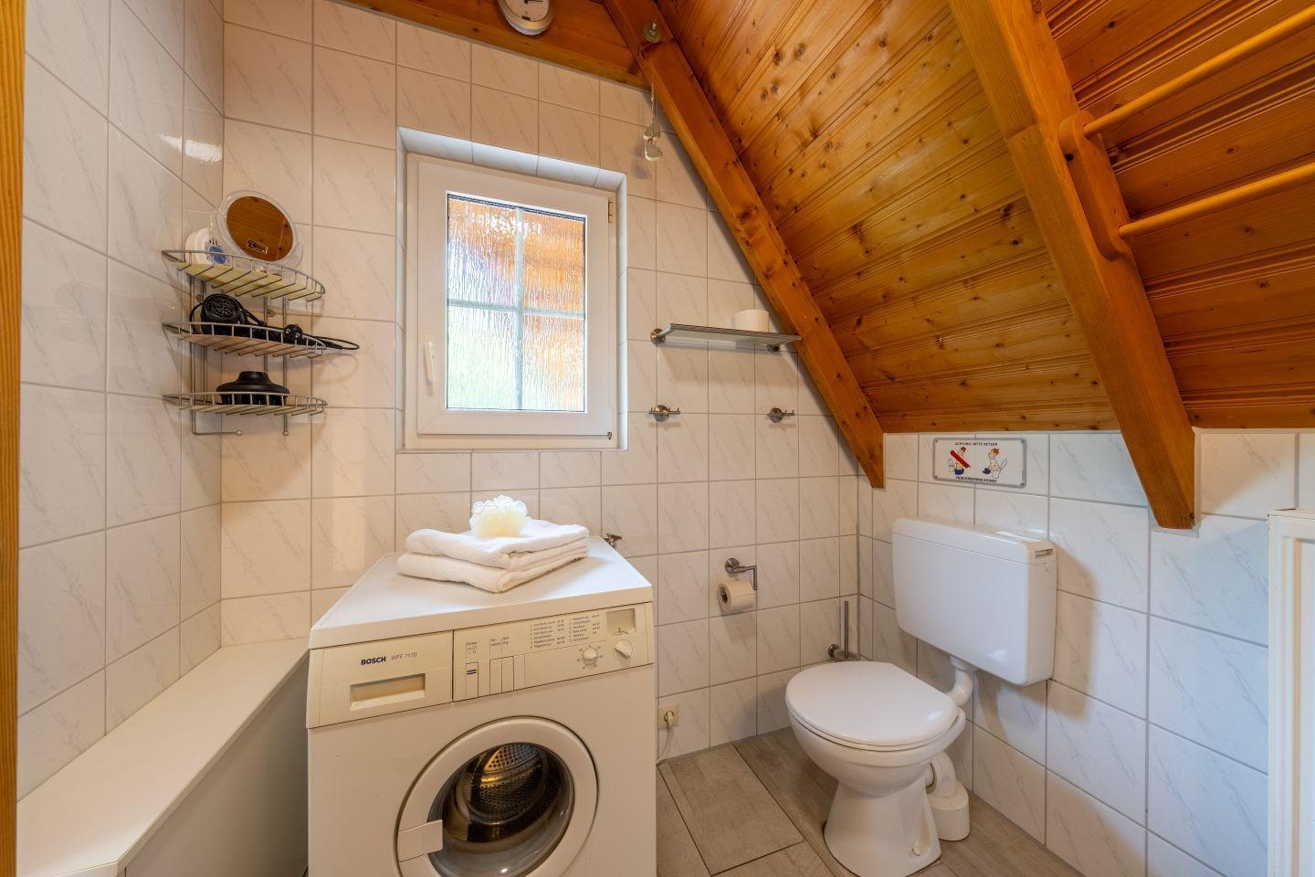 Bathroom with washing machine, toilet, and skylight under wooden ceiling.