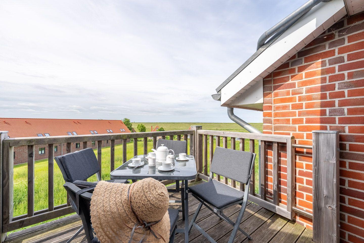 Terrasse mit Tisch, Stühlen und Teeservice. Blick auf grüne Wiesen und rote Dächer.