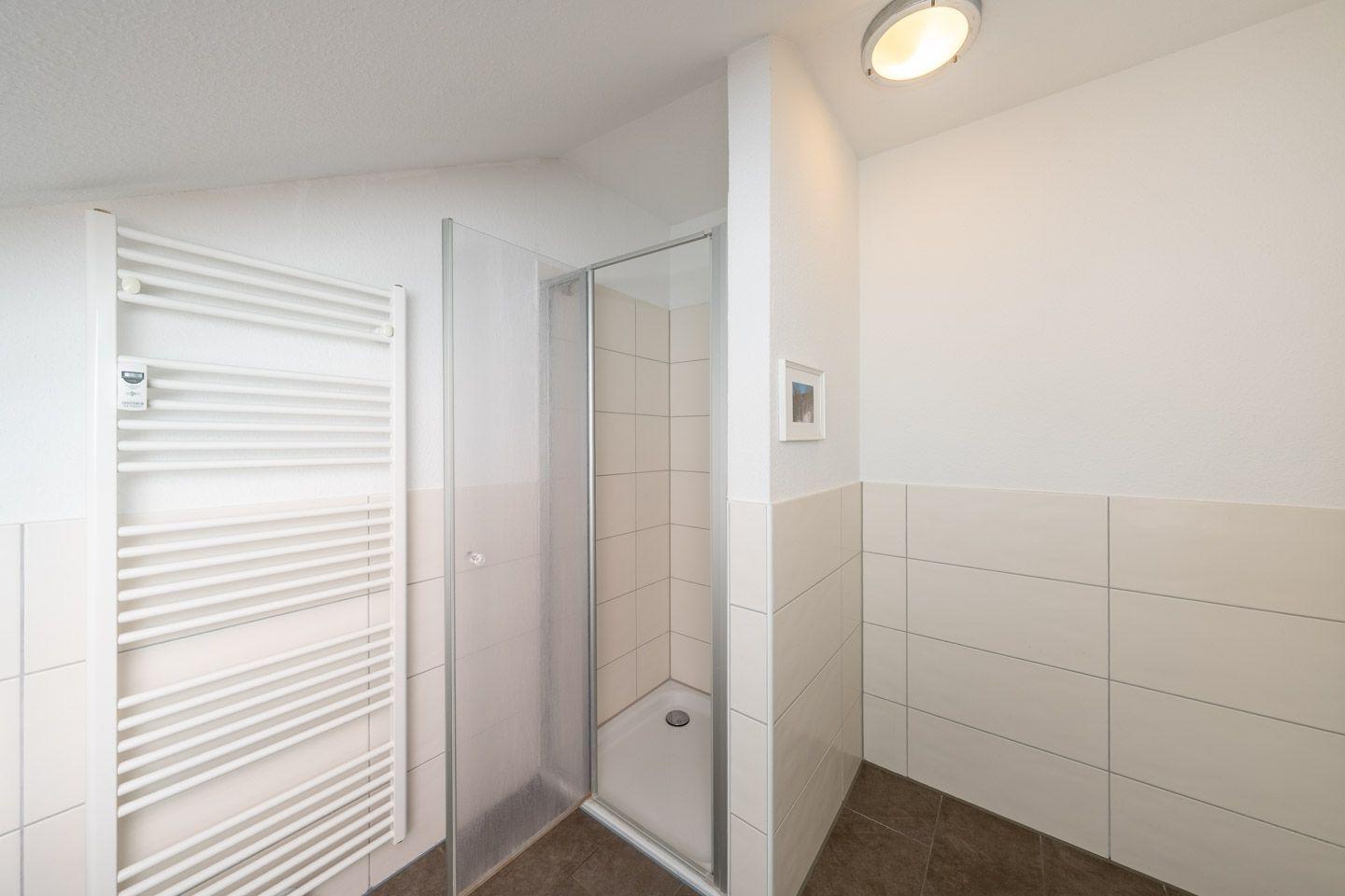 Badezimmer mit Dusche und Heizkörper an der Wand.