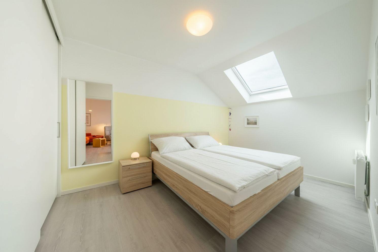Schlafzimmer mit Dachschräge, Dachfenster und Holzbett. Nebenraum sichtbar.